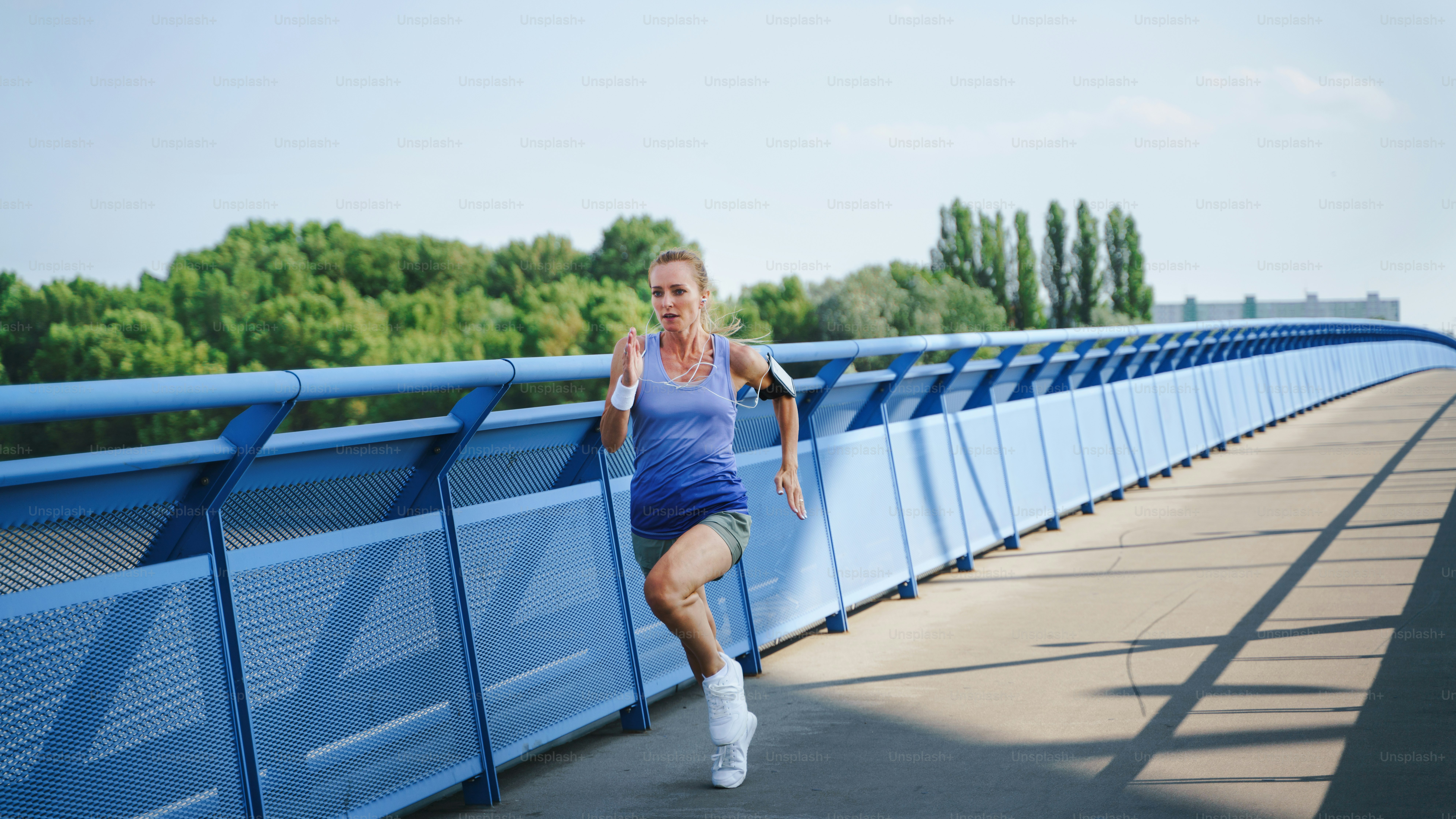 A mid adult woman runner stretching outdoors on bridge in city, healthy ...