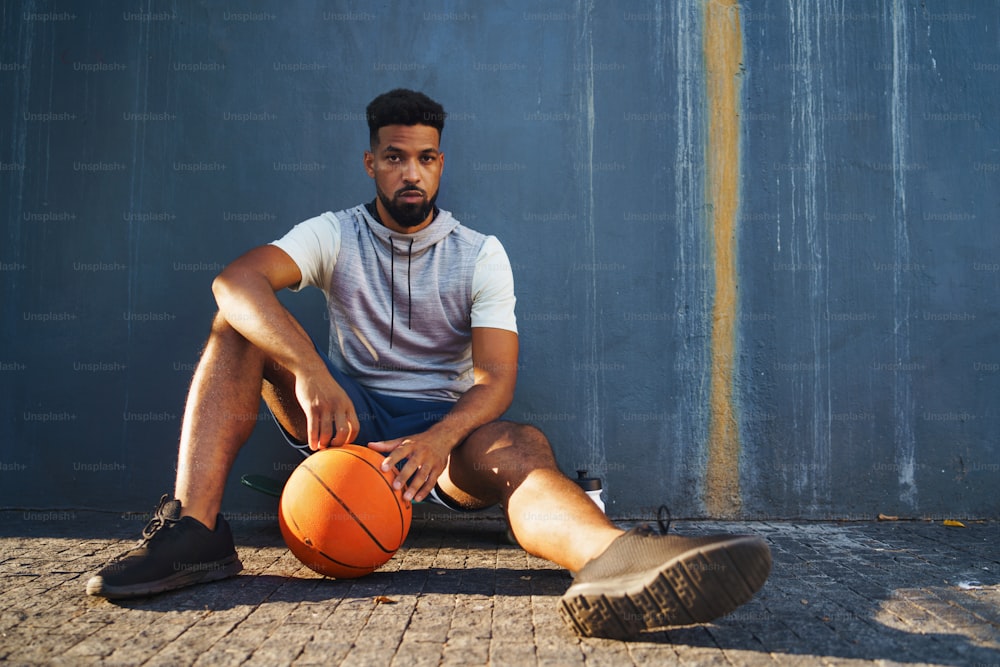 농구를 한 청년이 도시에서 야외에서 운동을 하고 앉아서 쉬고 있습니다.