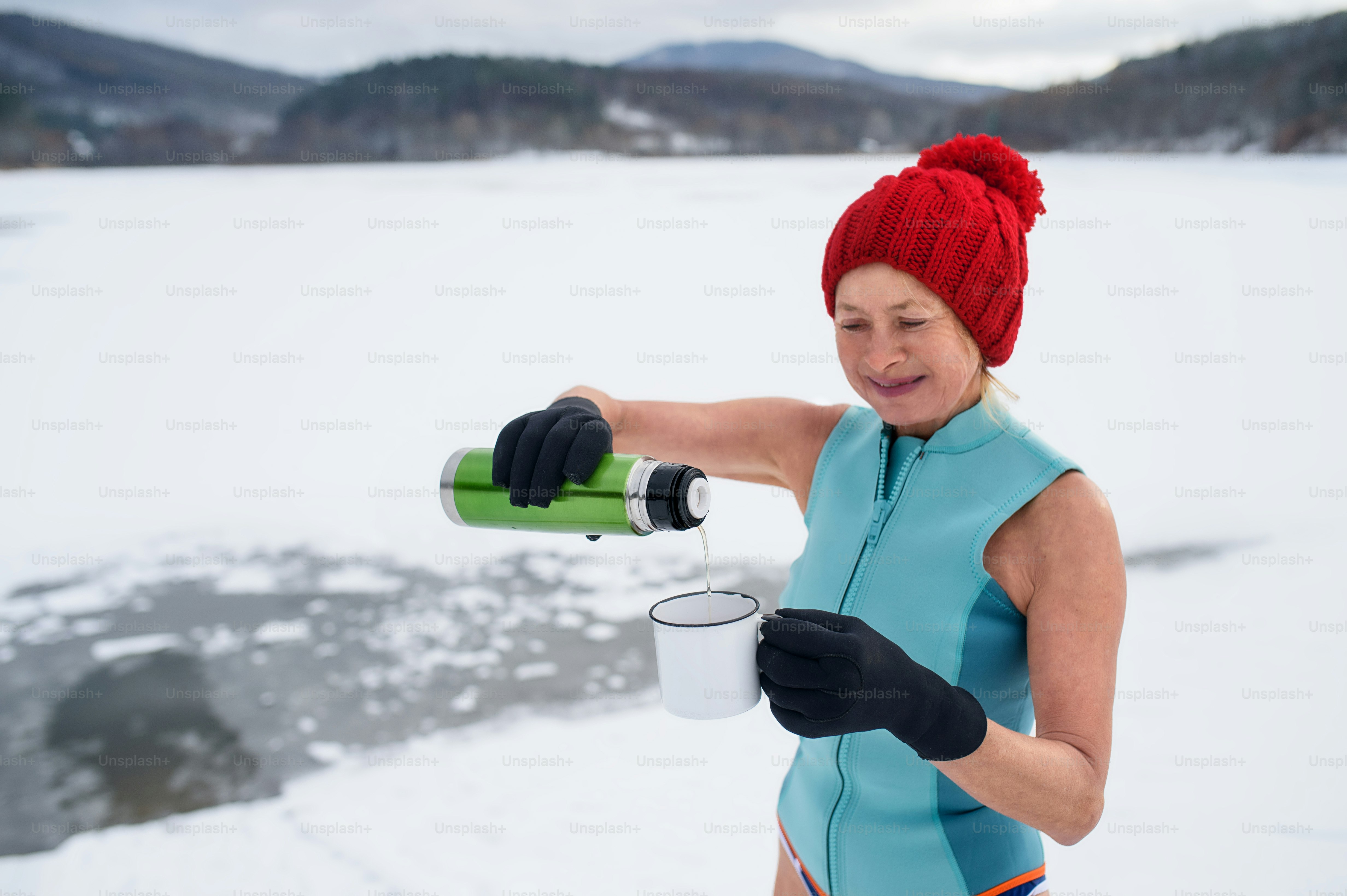 Eine aktive Seniorin im Badeanzug, die im Winter Tee im Freien trinkt, Kältetherapiekonzept