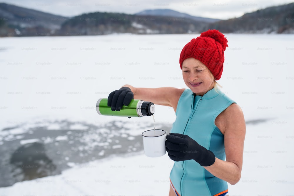 Eine aktive Seniorin im Badeanzug, die im Winter Tee im Freien trinkt, Kältetherapiekonzept.