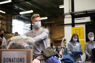 Portrait of volunteers sorting out donated clothes in community charity donation center, coronavirus concept.