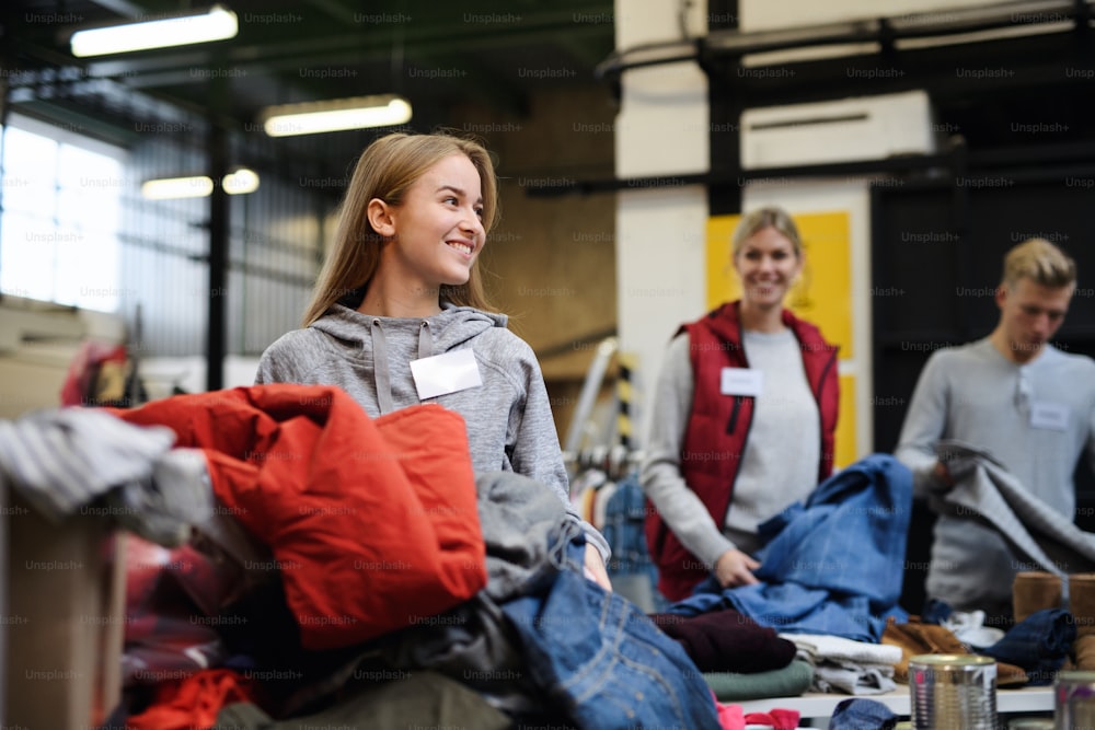 Portrait of volunteers sorting out donated clothes in community charity donation center.