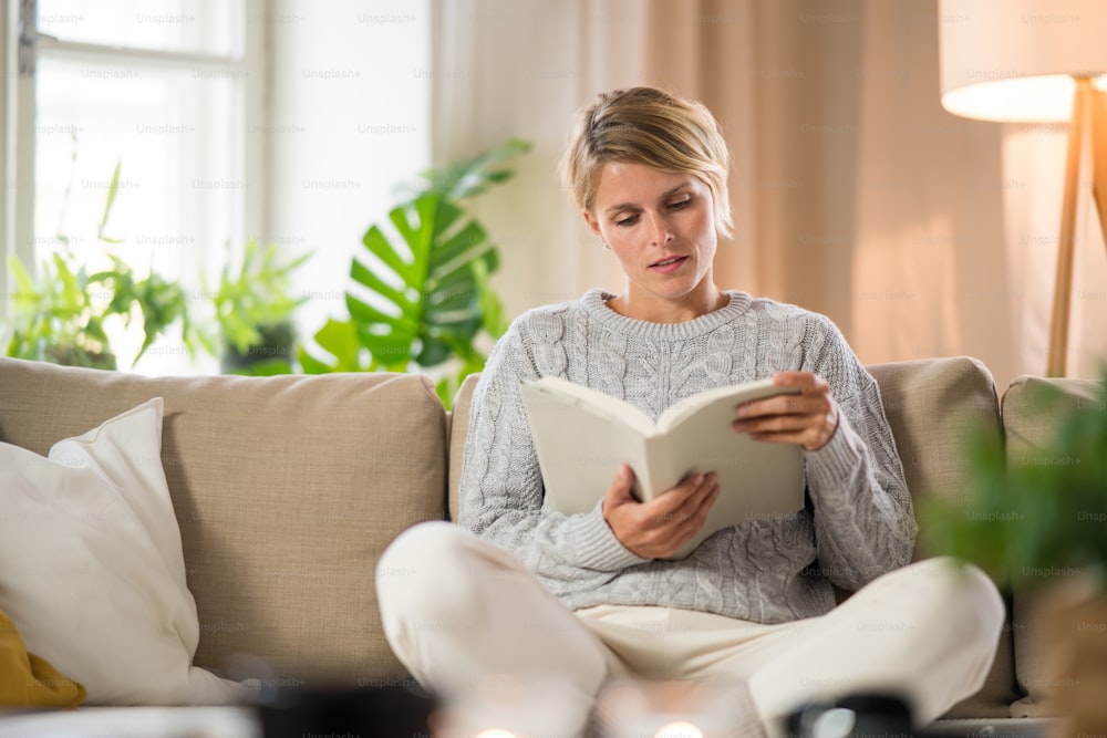 Retrato de vista frontal de mujer relajándose y leyendo libro en el interior de la casa, concepto de atención de la salud mental.