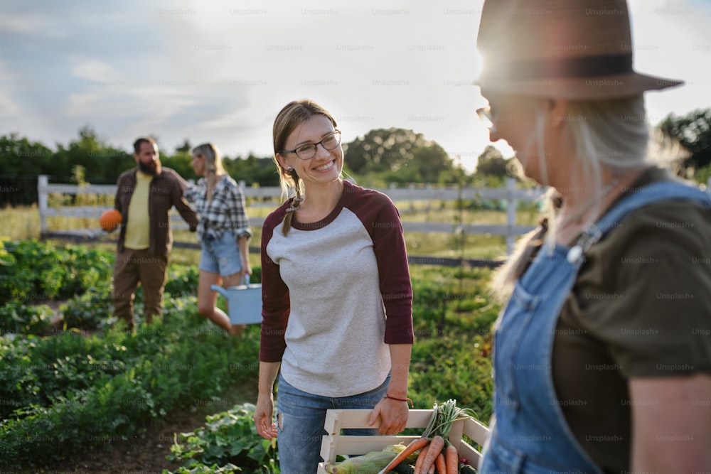Feliz granjera adulta de mediana edad abrazando a su compañera mayor sosteniendo una canasta con verduras de cosecha propia al aire libre en una granja comunitaria.
