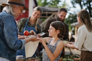 Una niña pequeña comprando verduras orgánicas al aire libre en el mercado comunitario de agricultores.
