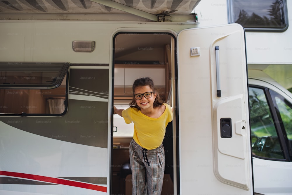 Uma garotinha feliz de pé na porta da caravana, olhando para a câmera. Viagem de férias em família.