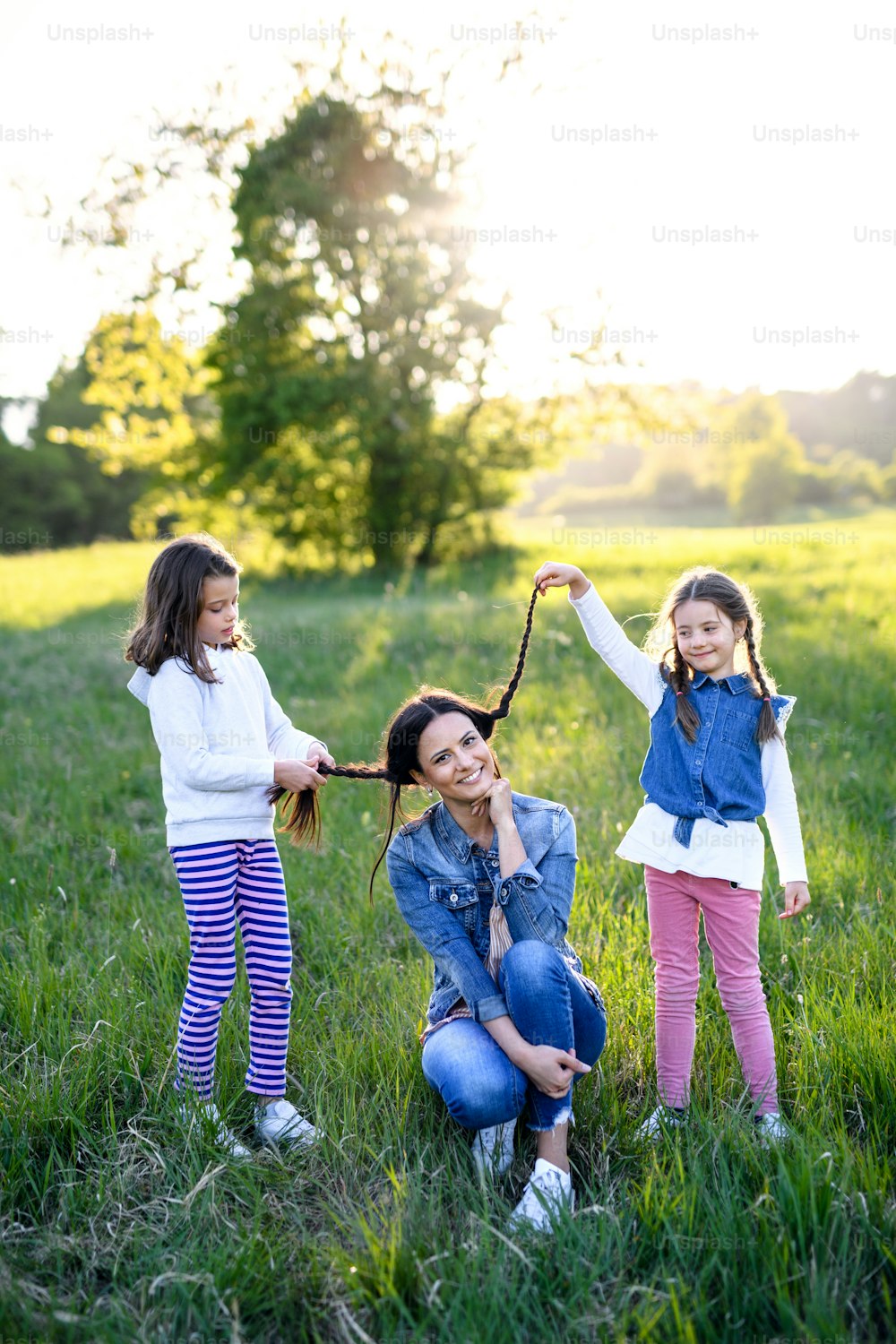 Vista frontal de la madre con dos hijas pequeñas divirtiéndose al aire libre en la naturaleza primaveral, jugando con el cabello.