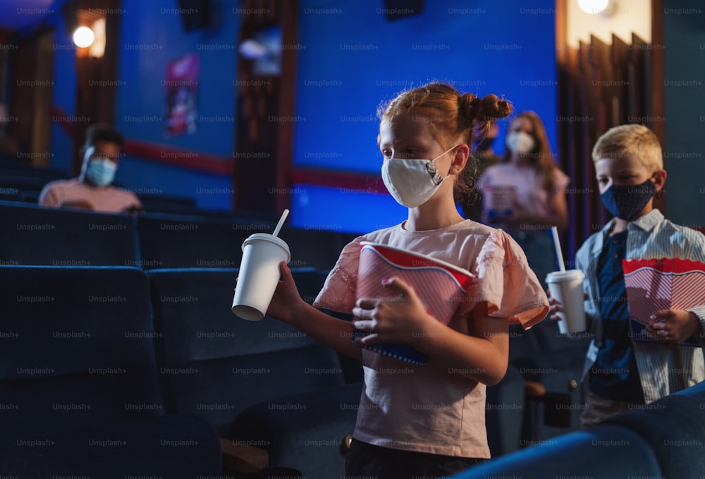 Happy small children with popcorn walking in the cinema, a coronavirus concept.