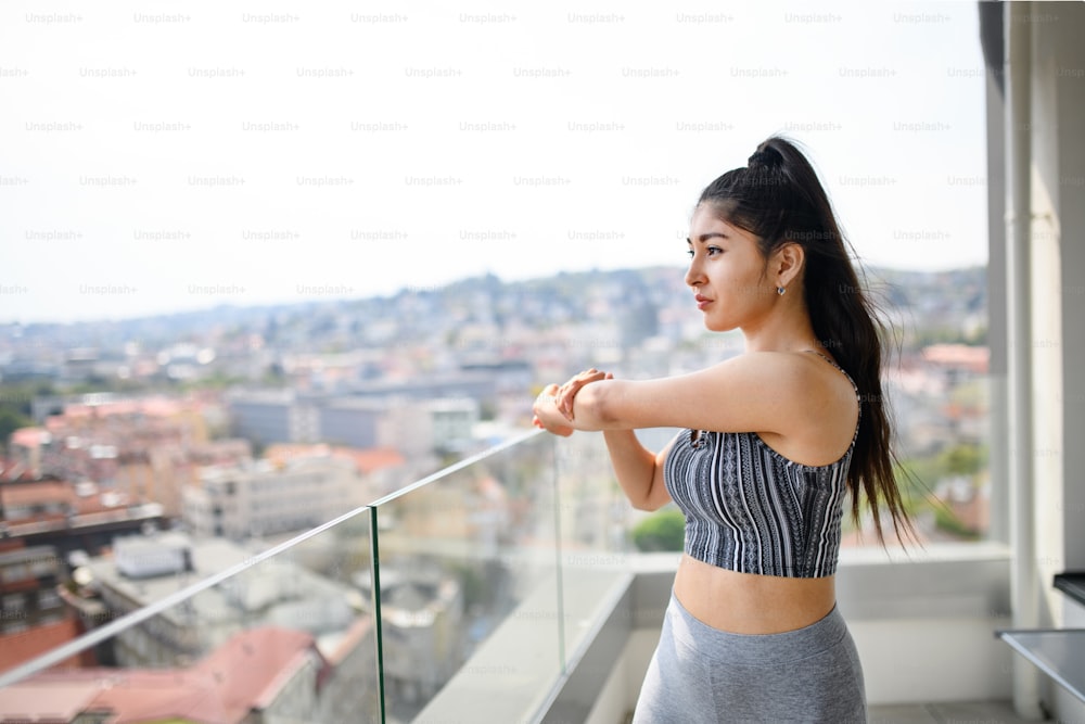 A portrait of young sport woman doing exercise on balcony outdoors in city, stretching.