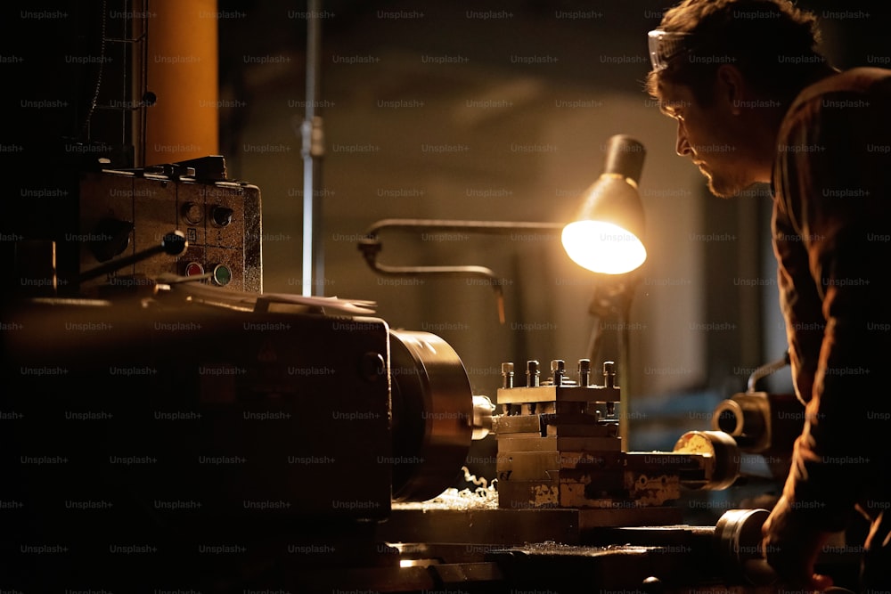 An industrial man working indoors in metal workshop at night.