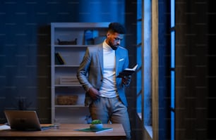 Ein junger afroamerikanischer Geschäftsmann, der nachts drinnen im Büro auf das Tagebuch schaut.