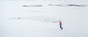 A very long shot of active senior woman running outdoors in snowy winter. Copy space.