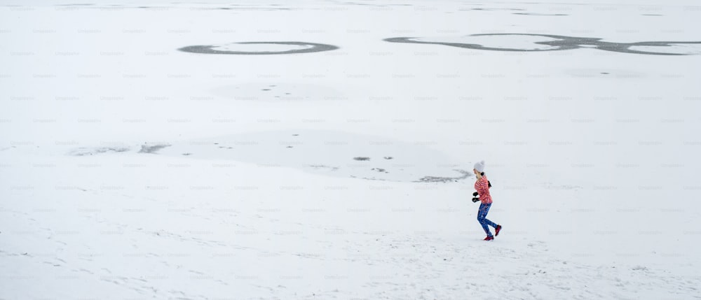 Un'inquadratura molto lunga di una donna anziana attiva che corre all'aperto nell'inverno nevoso. Copia spazio.