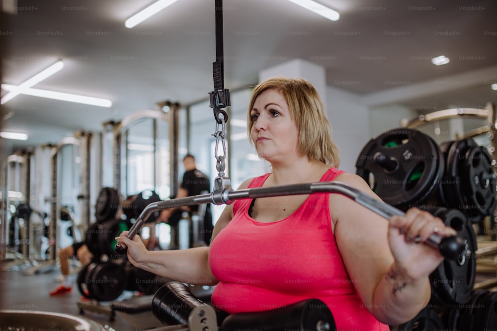 Uma mulher plus size adulta média que se exercita em uma máquina pulldown lat dentro de casa na academia