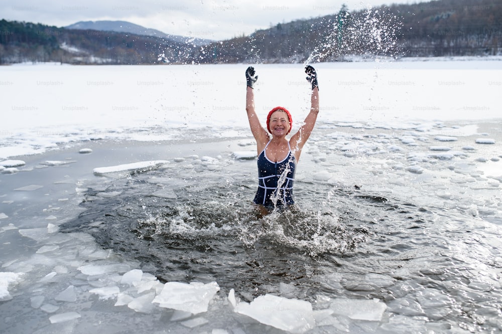 겨울에 야외에서 물을 튀기는 수영복을 입은 활동적인 노인 여성의 전면 모습, 차가운 치료 개념.