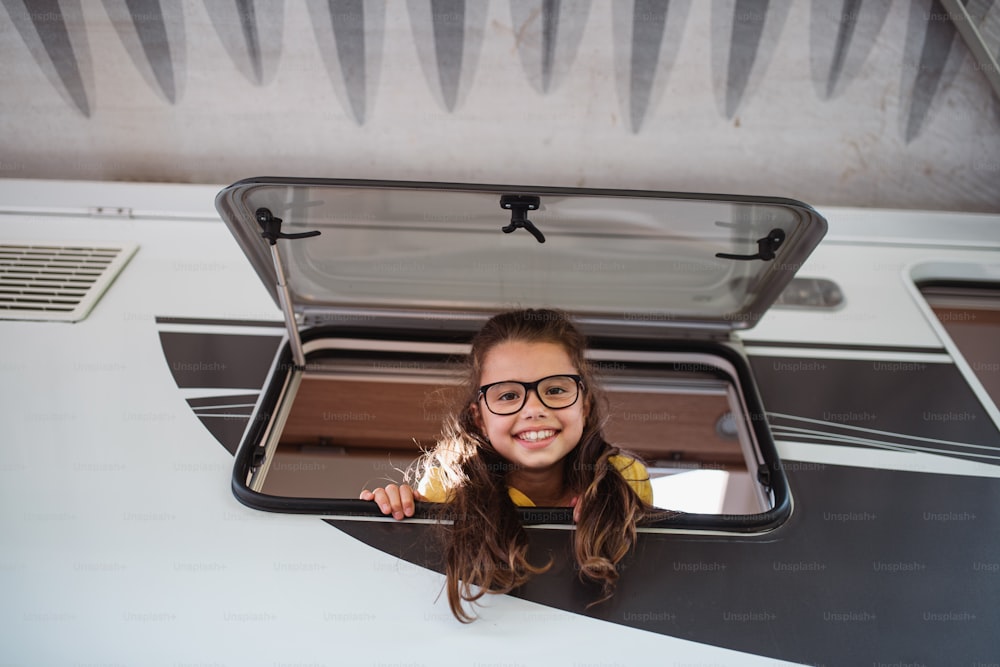캐러밴 창문을 통해 밖을 내다보고 카메라를 바라보는 행복한 작은 소녀, 가족 휴가 여행.