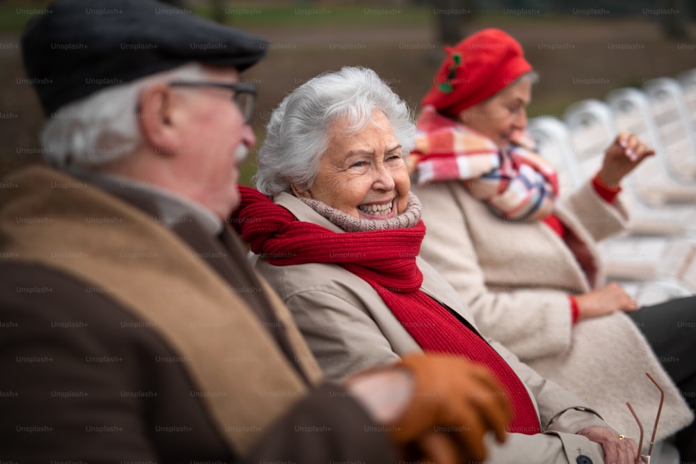 A group of happy senior friends sitting on bench in town park in autumn.