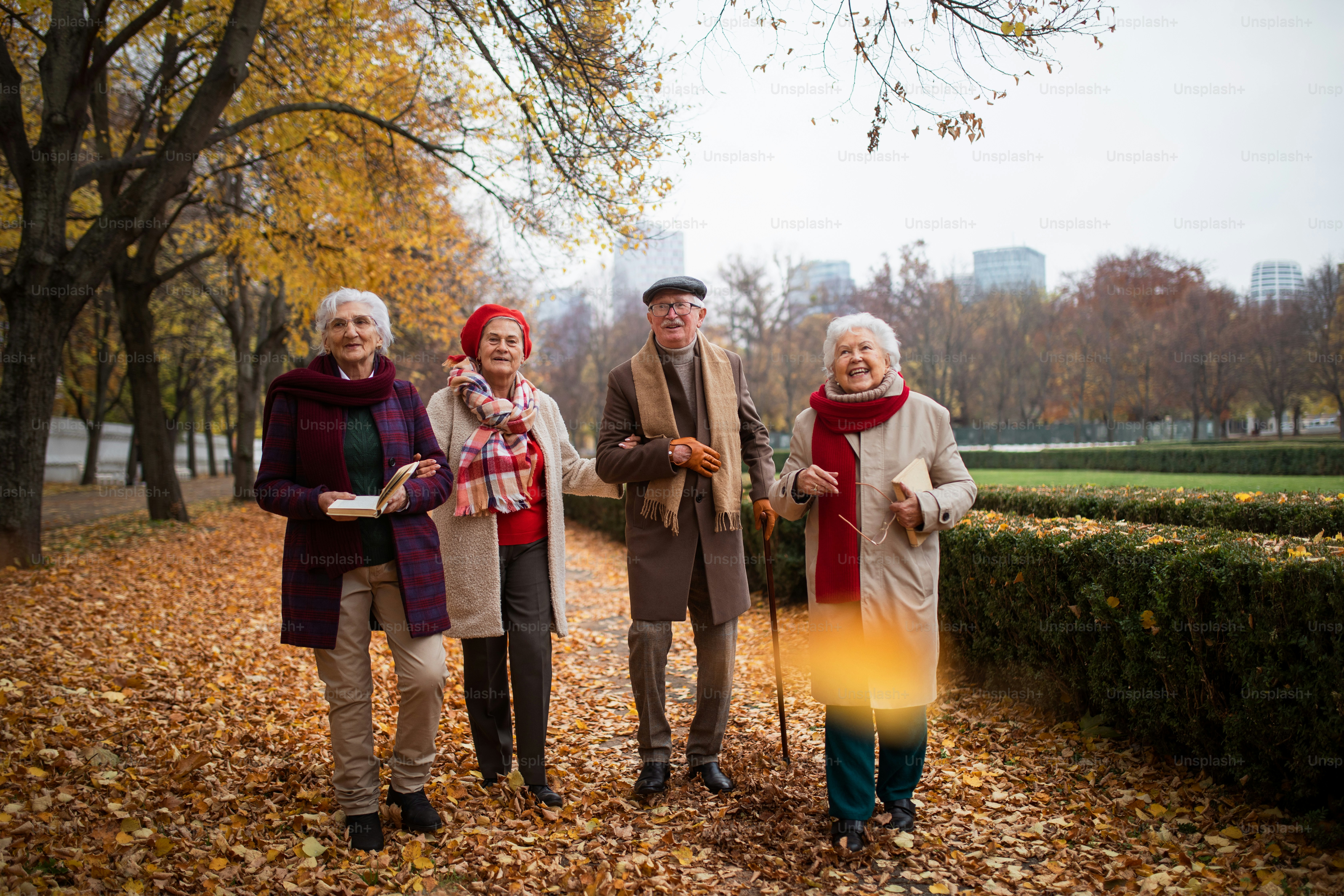 Un grupo de amigos mayores felices con libros sobre caminar al aire libre en el parque en otoño, hablando y riendo