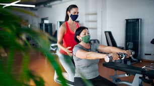 Active senior woman with personal trainer doing exercise in gym, coronavirus concept.