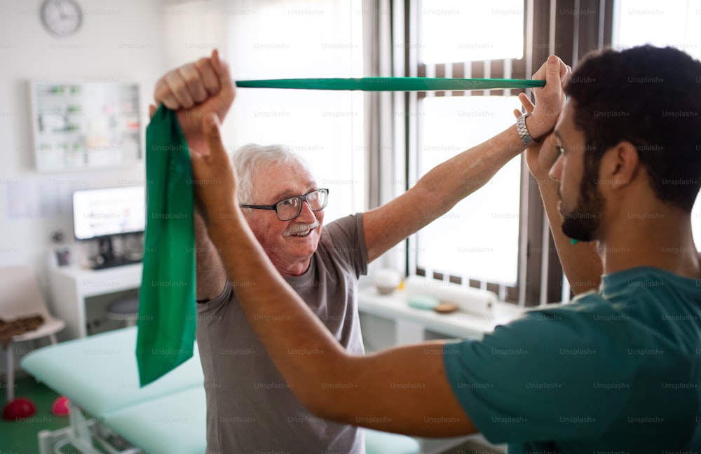 Un jeune kinésithérapeute fait de l’exercice avec un patient âgé dans une salle de physique