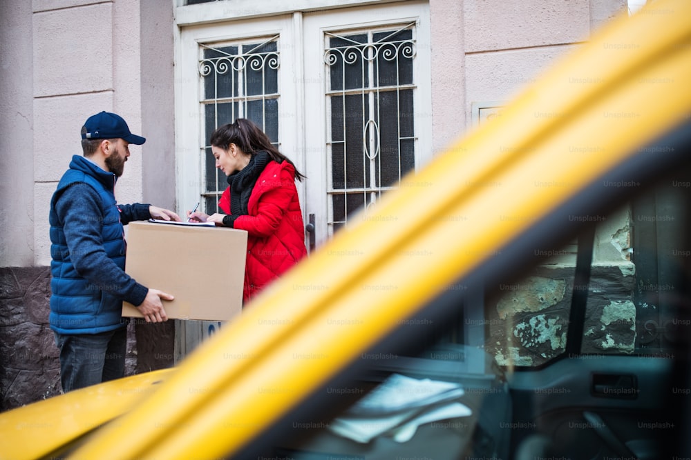 Young woman receiving parcel from delivery man at the door - courier service concept.