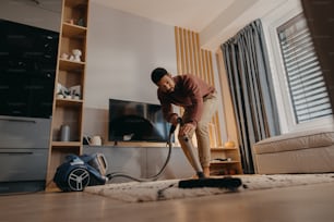 A young man hoovering carpet with vacuum cleaner in living room