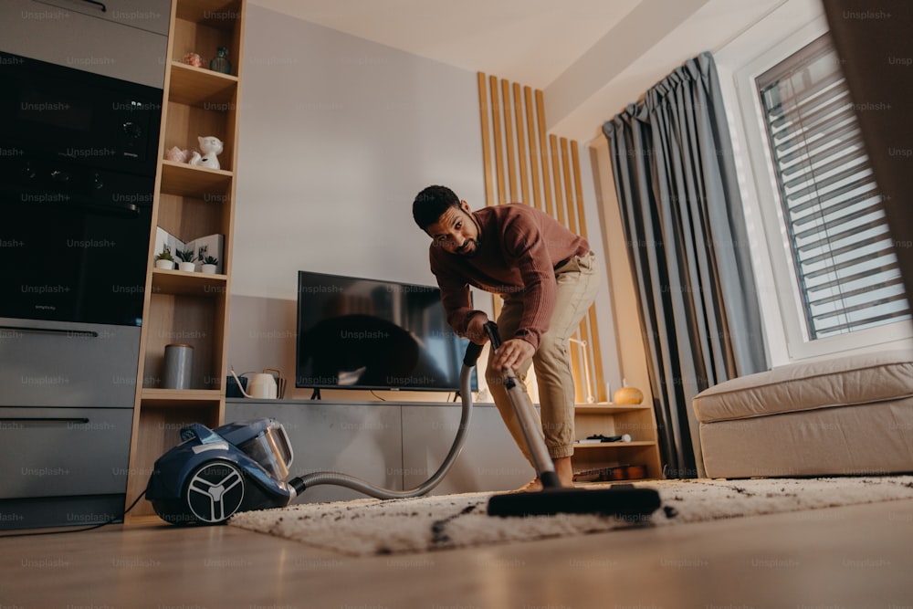 A young man hoovering carpet with vacuum cleaner in living room