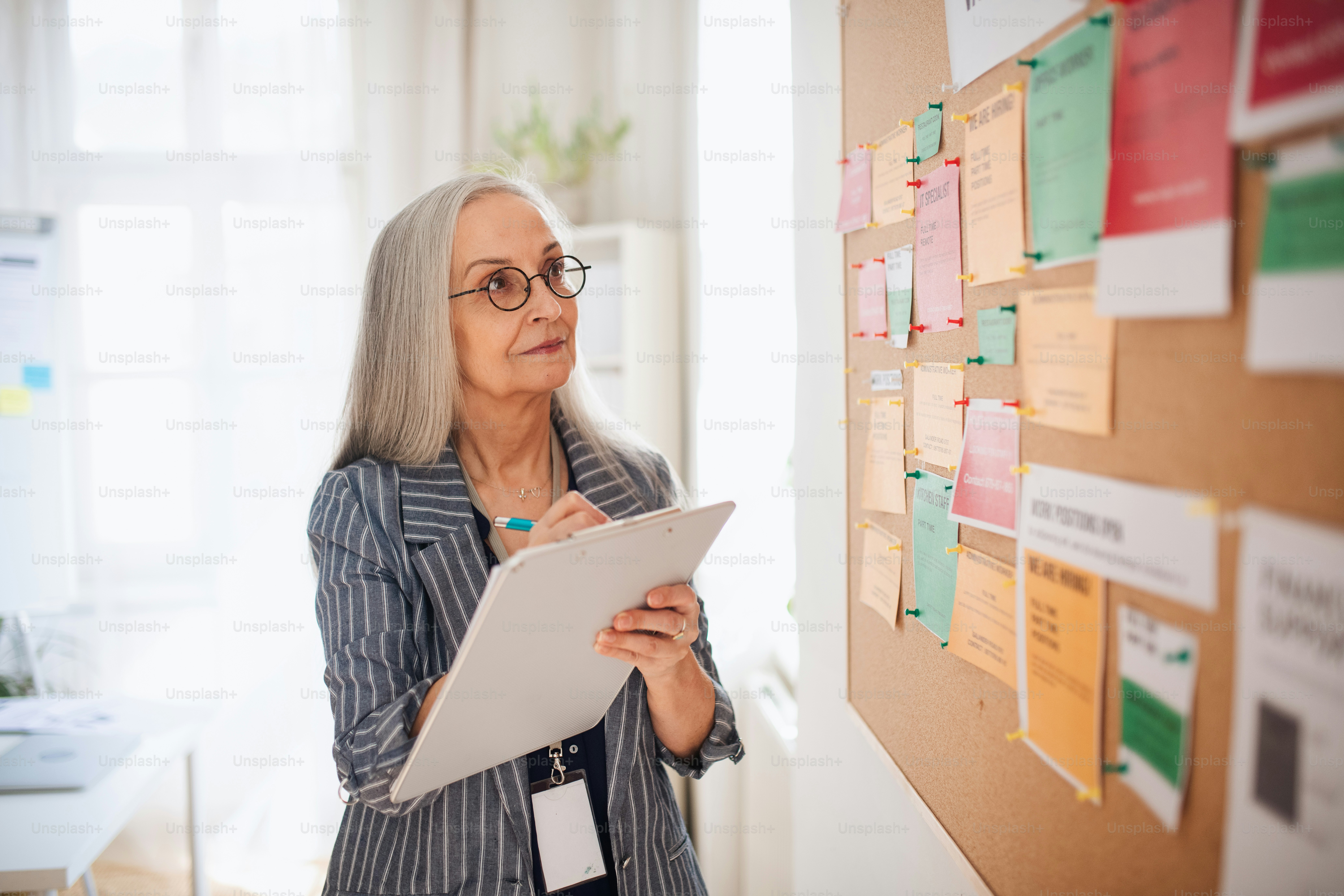 A job center employee with file form standing in front of employment noticeboard.