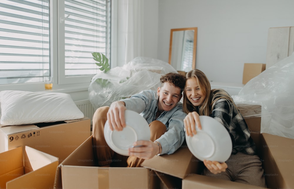 Una alegre pareja joven en su nuevo apartamento, divirtiéndose al desempacar. Concepción de la mudanza.