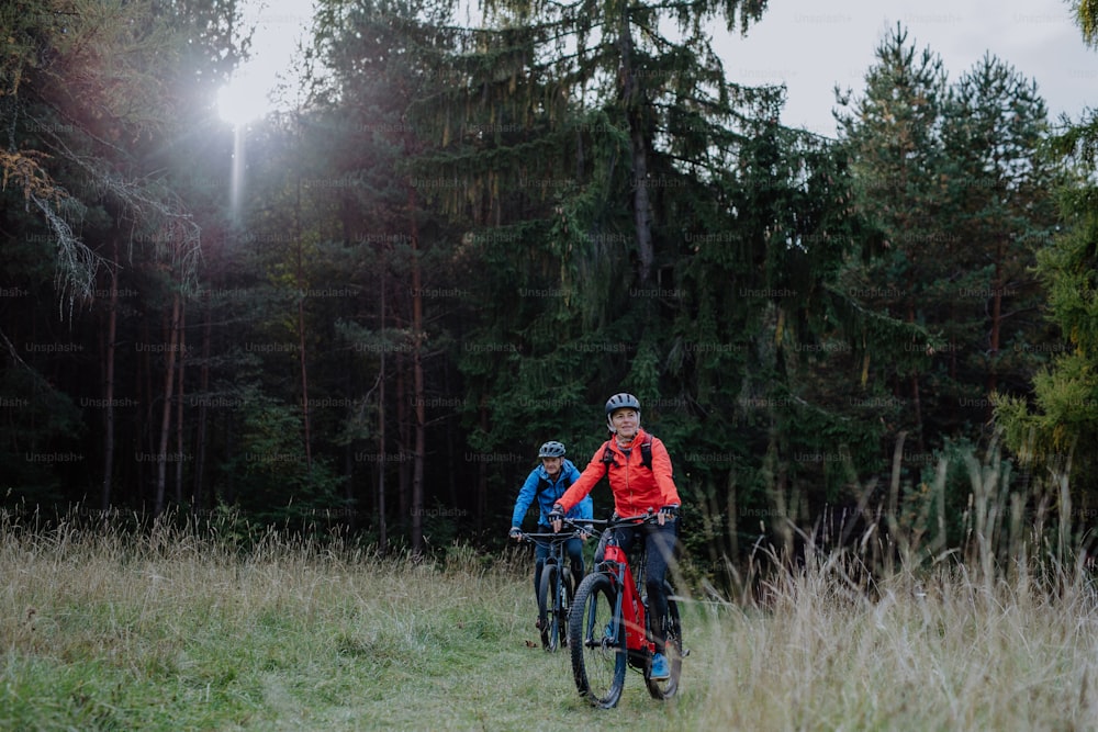 An active senior couple riding bikes outdoors in forest in autumn day.