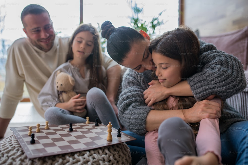 Zwei glückliche Schwestern mit Mutter und Vater, die auf dem Boden sitzen und zu Hause zusammen Schach spielen