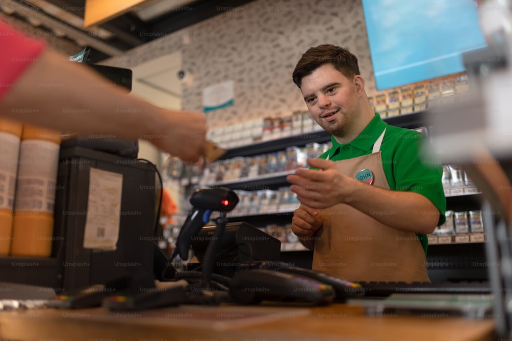 Un joven y alegre empleado con síndrome de Down que recibe el pago en efectivo del cliente en la cafetería de la gasolinera.