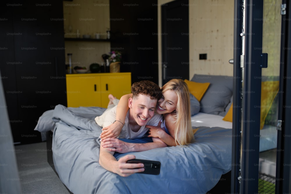 タイニーハウスの新しい家で朝ベッドに横たわっている愛の若い幸せなカップル、持続可能な生活のコンセプト。