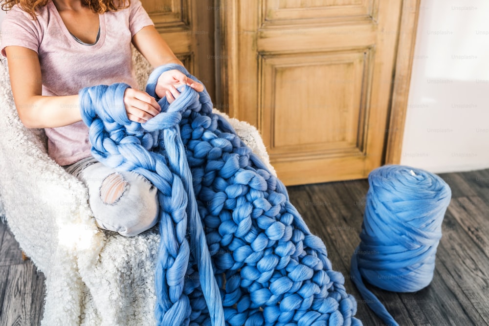 Kleinbetrieb einer jungen Frau. Nicht erkennbare Frau, die eine Wolldecke von Hand strickt.