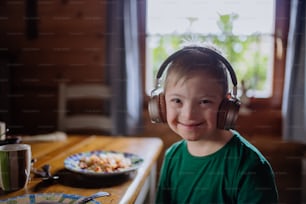 A boy with Down syndrome having lunch with headphones and looking at camera at home.