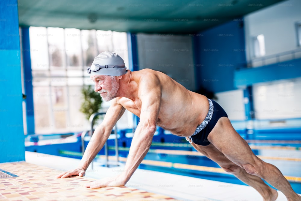 Uomo anziano in piedi vicino alla piscina coperta, stretching. Pensionato attivo che ama lo sport.
