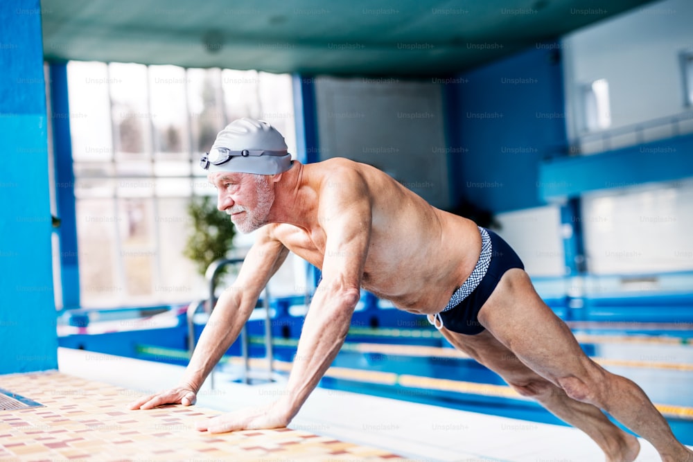 Senior man standing by the indoor swimming pool, stretching. Active pensioner enjoying sport.