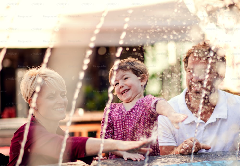 Parents with two small daugther having fun outdoors by fountain in town.