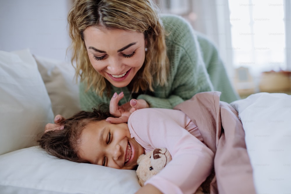 A happy mother stroking her little daughter when waking her up in morning.