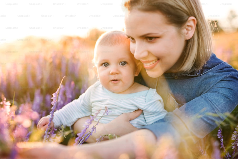 Schöne junge Mutter, die ihren kleinen Sohn in den Armen hält, draußen in der Natur im Lavendelfeld.