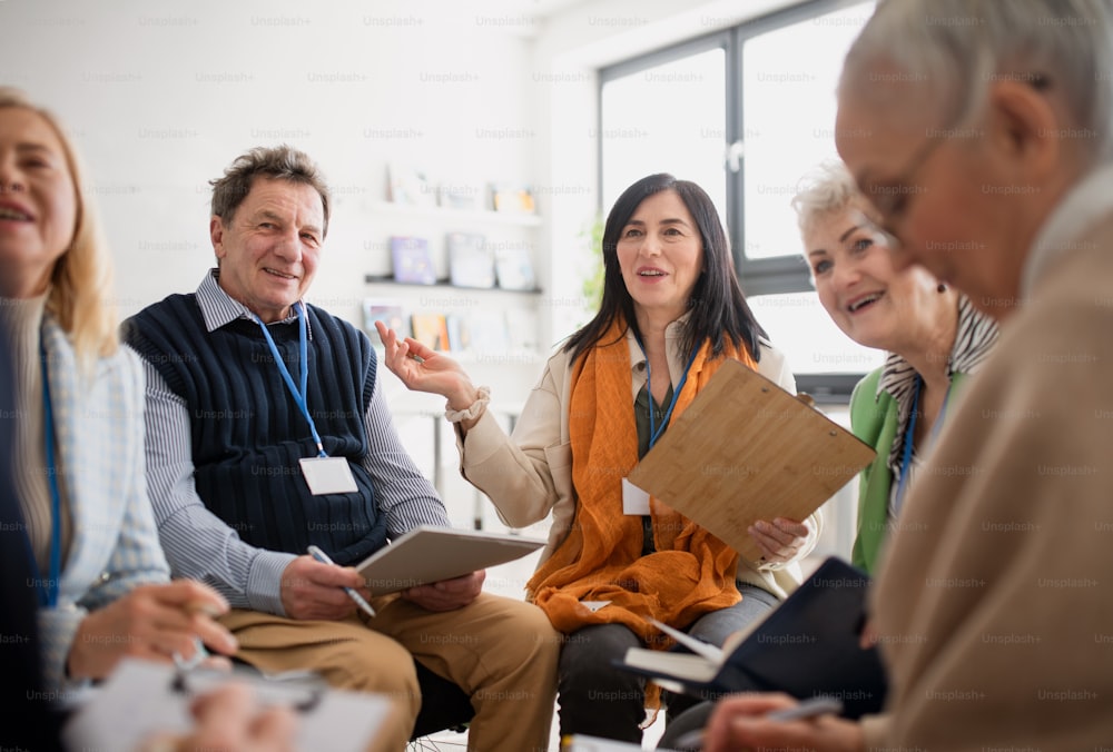 Des personnes âgées excitées assistant à une séance de thérapie de groupe dans une maison de retraite, un homme et une femme âgés positifs assis en cercle, ayant une conversation avec un psychologue
