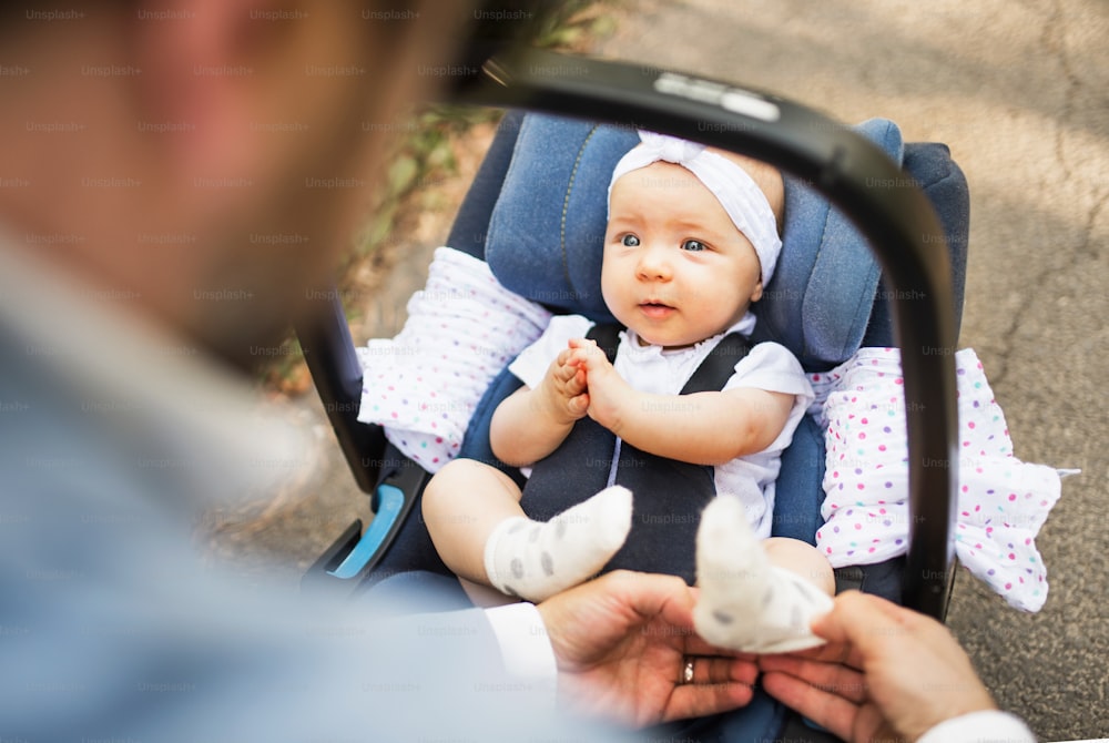 Unrecognizable father outdoors with his cute baby daughter sitting in car safety seat.