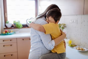 A happy young mother hugging her little son in kitchen at home.