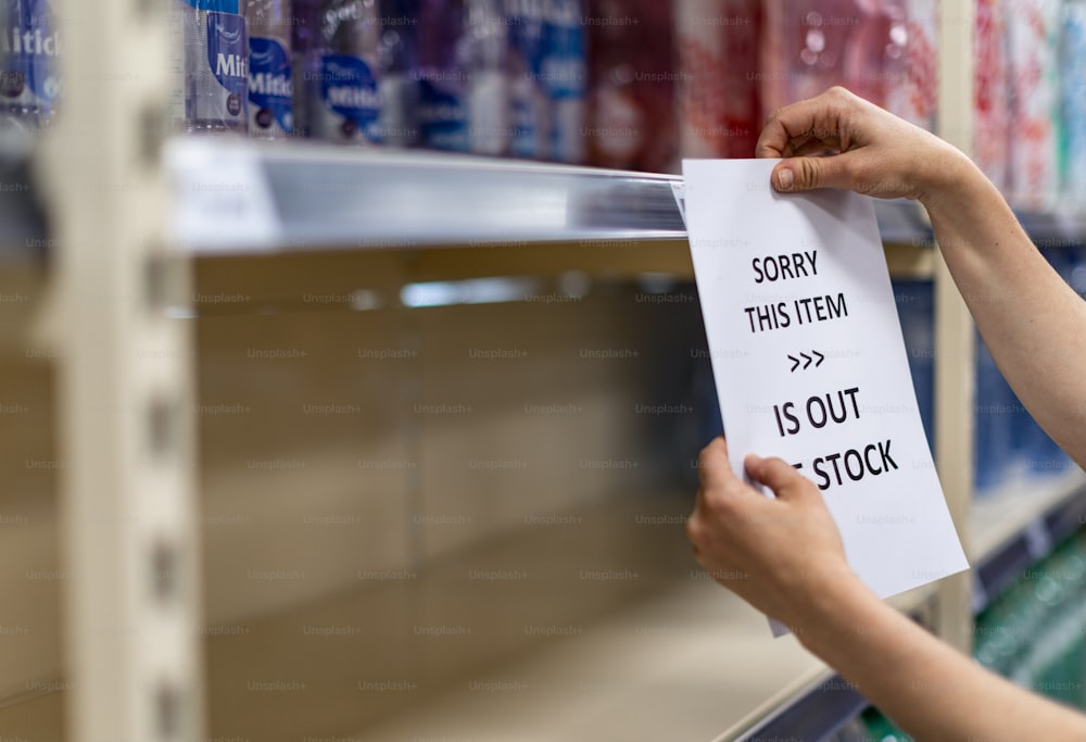 Shop assistant hanging notification of sold out goods in empty shelves in a grocery store