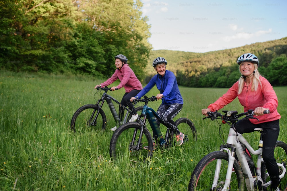 Happy active senior women friends cycling together outdoors in the nature.