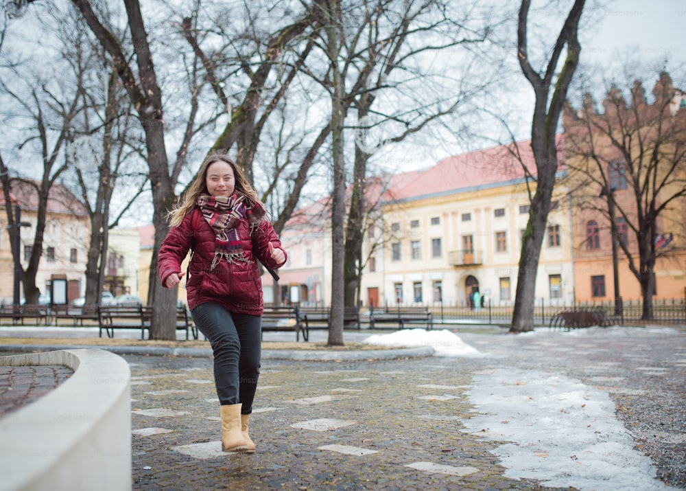 A happy young woman student with Down syndrome running in street in winter
