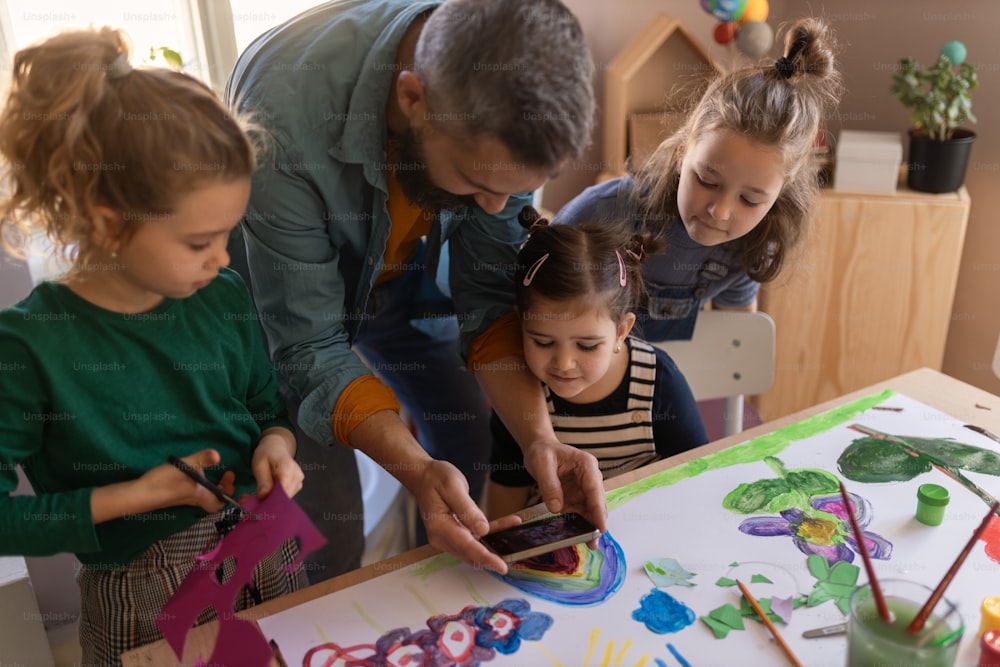学校の屋内で創造的なアートとクラフトのクラスで教師と一緒にプロジェクトに取り組んでいる小さな子供たちのグループ。