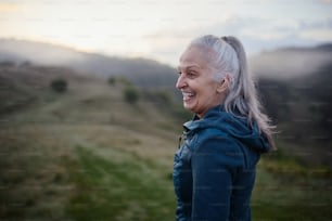 A senior woman hiking in nature on early morning with fog and mountains in background.