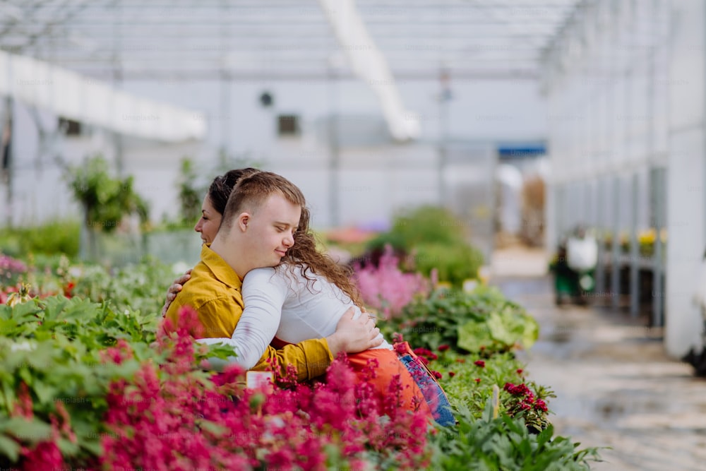 A woman florist hugging her young colleague with Down syndrome in garden centre.
