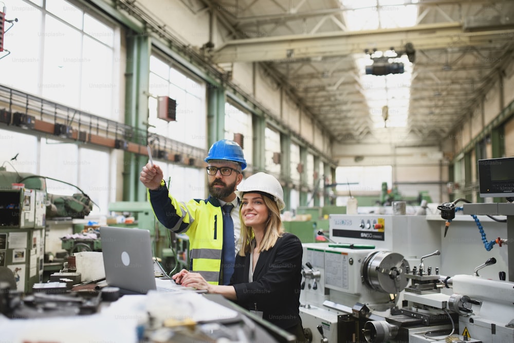 Un uomo e una donna ingegneri industriali discutono del nuovo progetto di macchinari della fabbrica e dell'utilizzo del laptop.